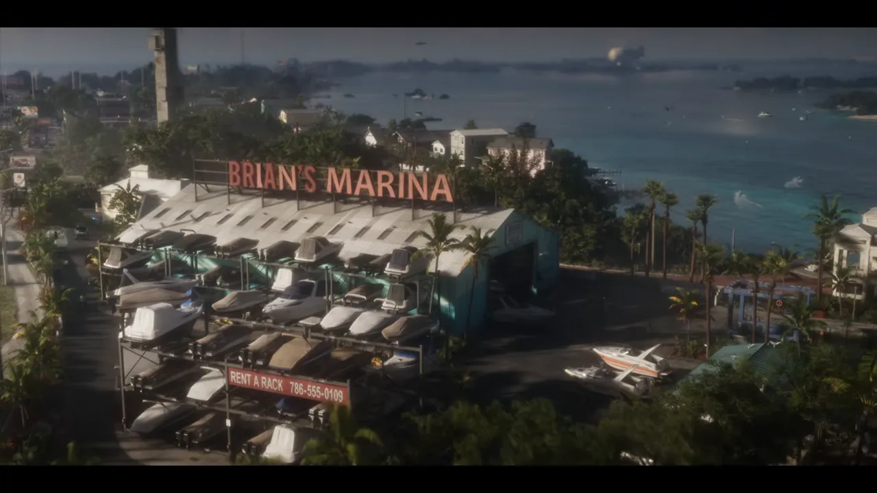 Vue aérienne d'une marina : enseigne « BRIAN'S MARINA » sur un hangar, bateaux empilés sur des racks, panneau « RENT A RACK » au bas des racks, mer turquoise et côte au fond.